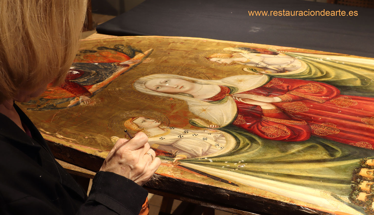 fotografia de la restauradora de pintura sobre tabla durante el proceso de restauración del fondo dorado.